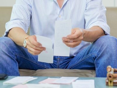 Concentrated man sitting before receipts on the table and analyzing his income and expenses at his home